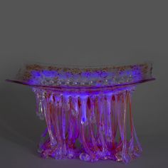 a glass table with pink and purple lights on it's sides, in front of a gray background