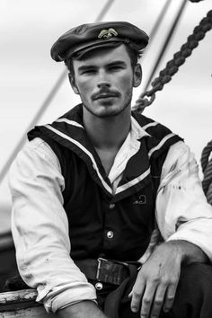 a man sitting on top of a boat wearing a sailor's hat and vest