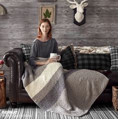 a woman sitting on a couch with a blanket over her and holding a coffee cup