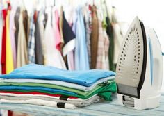 an iron is sitting on top of some folded shirts in front of the ironing board