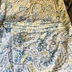 the bed is covered with a blue and yellow paisley print comforter set on top of a wooden table