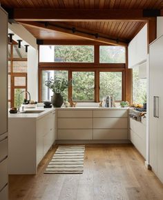 a kitchen with wooden ceiling and white cabinetry next to a large window overlooking the trees