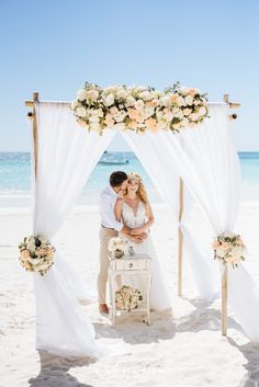 a bride and groom kissing under an arch on the beach