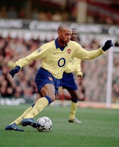 a man kicking a soccer ball on top of a field with people in the background