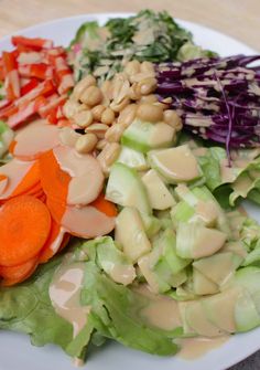 a white plate topped with lettuce, carrots and other veggies