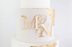 a white and gold wedding cake with the letter m on it's top tier