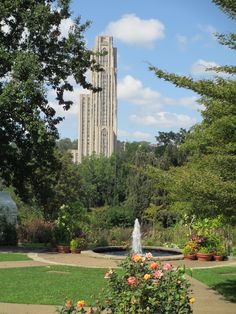 a tall building with a fountain in the middle of it and lots of trees around it