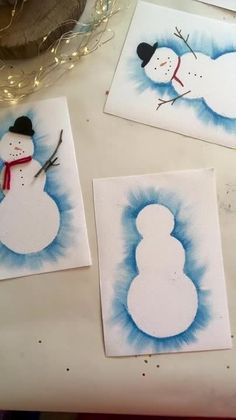 three snowmen painted on white paper sitting on a table