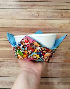 a hand holding a paper bowl with cartoon characters on it