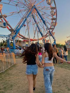 two girls walking towards a ferris wheel at an amusement park