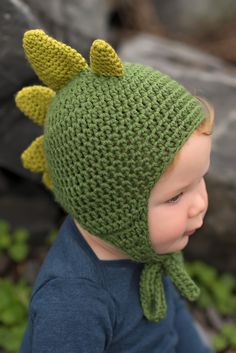 a small child wearing a knitted green hat with yellow horns and ears on it's head