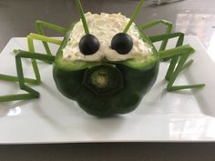 a green pepper topped with whipped cream and black googly eyes on a white plate