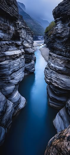 a river flowing between two large rocks in the middle of a mountain range at dusk