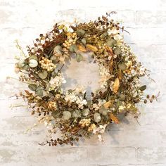 a wreath with dried flowers and leaves hanging on a brick wall