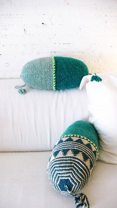 two knitted pillows sitting on top of a white couch next to a pillow with tassels