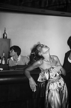 an old photo of a woman dancing in front of two men at a bar with drinks on the table