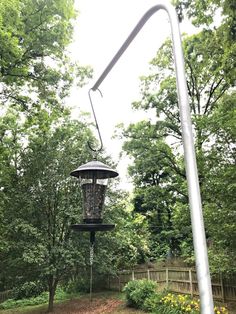 a bird feeder hanging from the side of a metal pole next to trees and flowers