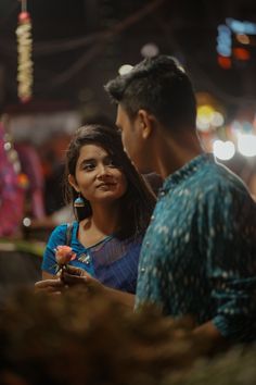 a man standing next to a woman holding a rose in her hand and looking at the camera