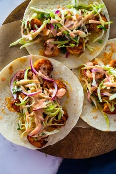 three fish tacos with cole slaw and mayonnaise on a cutting board