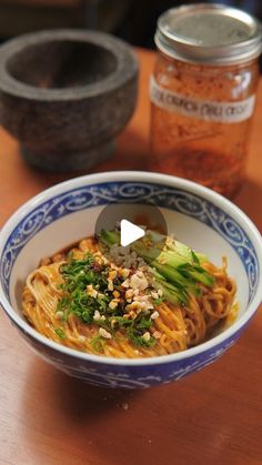 a bowl filled with noodles and vegetables on top of a wooden table next to jars