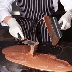 a person in an apron and white gloves is using a spatula to paint a piece of metal