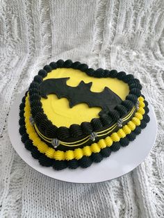 a batman cake with yellow and black icing on a white platter next to a white knitted blanket