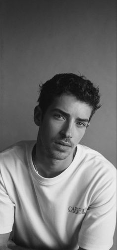 a black and white photo of a man in a t - shirt sitting at a table