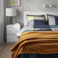 a bed with yellow and blue sheets in a bedroom next to a white night stand