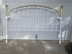 a white metal headboard with gold posts on the side of a garage door next to a driveway