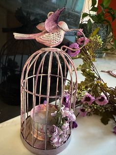 a pink bird sitting on top of a cage next to purple flowers and greenery