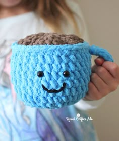 a crocheted coffee cup with a smiling face on it's side, held by a child