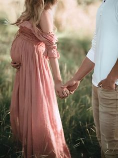 a man and woman holding hands while standing in tall grass