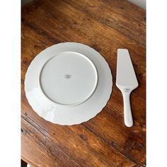 an empty white plate and knife on a wooden table next to a cutting utensil