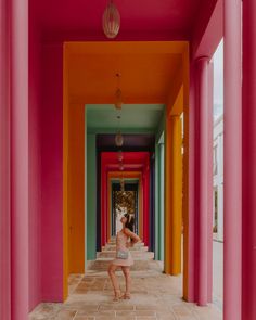 a woman is standing in the middle of a long hallway with bright colored columns on both sides