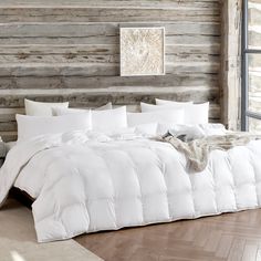 a bed with white comforter and pillows in a room next to a wooden wall