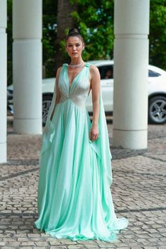 a woman in a long green dress is walking down the street with her hand on her hip