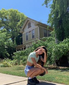 a woman kneeling down on the sidewalk in front of a house with her hand on her face