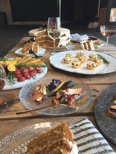 a wooden table topped with plates of food and desserts next to glasses of wine