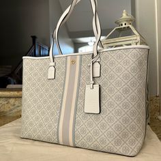 Tory Burch Geo Logo Tote Gray Gro With Stripe Coated Canvas With Leather Trim . Inside One Pocket . Magnetic Snap Closure, Unlined . Handles With 9" Drop . Brass/Gold Tone Hardware . Approx.: 15" (L) X 11 1/2" (H) X 5 3/4" (W) Features A Roomy Interior That Can Easily Accommodate All Of Your Everyday Essentials. Whether You’re Running Around Town Or Packing For A Weekend Get Away, It’s An Ideal Grab-And-Go Carryall For Any Time Of The Year. Holds A Full0 Day’s Essentials. Tory Burch Tote Bag, Tory Burch Tote, Tory Burch Bag Totes, Girly Bags, Luxury Purses, Pretty Bags, Tory Burch Bag, Brass Gold, Cute Bags