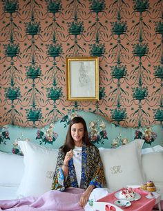 a woman sitting on top of a bed holding a cup