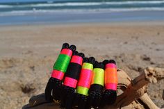 four colorful bracelets are on top of a piece of driftwood at the beach