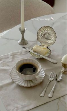 there is a cup of coffee on the table next to some silverware and a candle