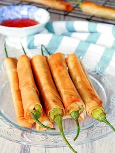 three spring rolls on a glass plate with peppers and ketchup in the background