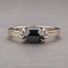 a black diamond ring sitting on top of a gray surface with an arrow shaped band