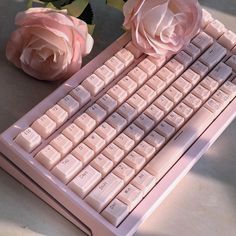 there is a pink keyboard and two roses on the table next to eachother