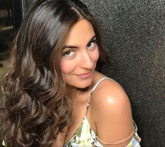 a woman with long brown hair posing for a photo in front of a gray wall