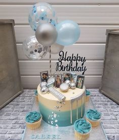 a birthday cake with blue frosting, balloons and pictures on the top is surrounded by other cupcakes