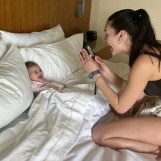 a woman sitting on a bed with a baby in her lap and an adult holding a cell phone