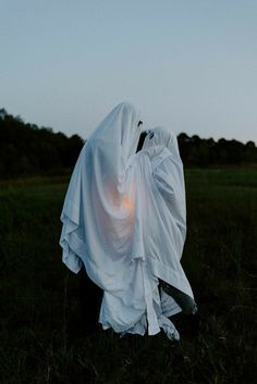 a ghostly person in a white cloth covering his face and head, standing in the grass