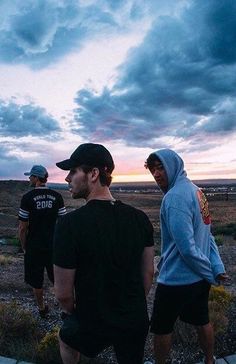 three men are standing on a wooden platform in the middle of an open field at sunset